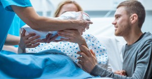 In the Hospital Midwife Gives Newborn Baby to a Mother to Hold, Supportive Father Lovingly Hugging Baby and Wife. Happy Family in the Modern Delivery Ward; blog: What Happens After You Give Birth?