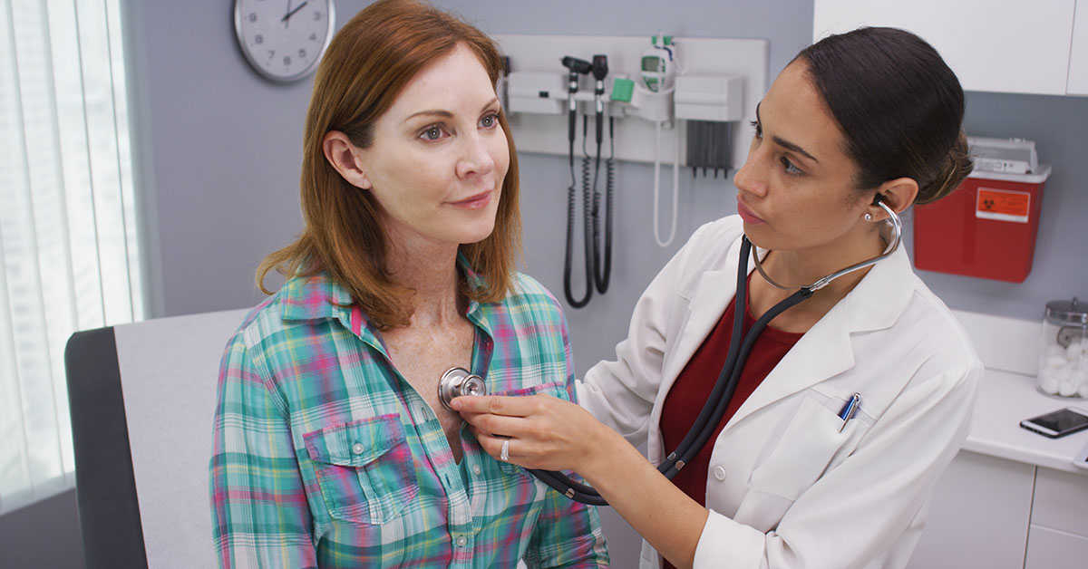 Lovely young latina doctor using stethoscope to examine senior patients vitals; blog: What is Preventive Healthcare?