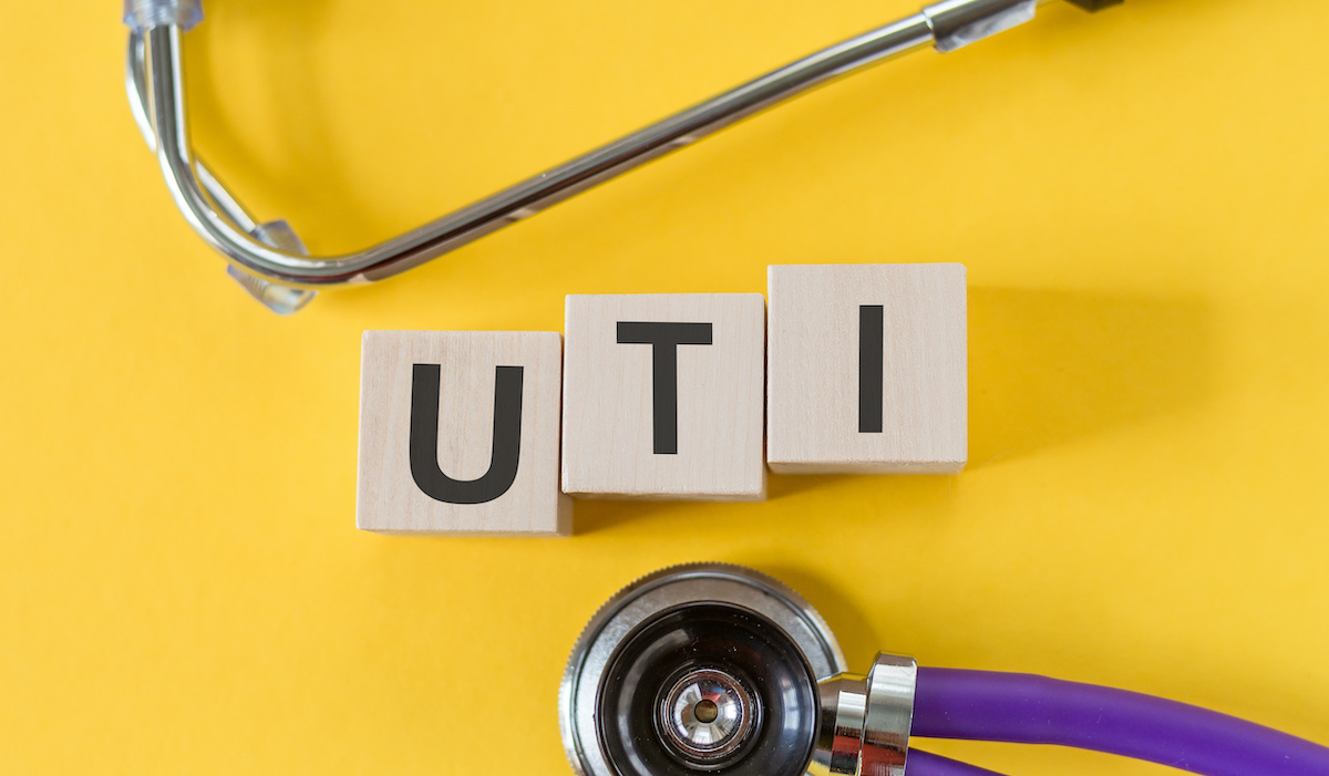 UTI - acronym from wooden blocks with letters, abbreviation UTI urinary tract infection, concept, yellow background with stethoscope; blog: Your Guide to UTIs